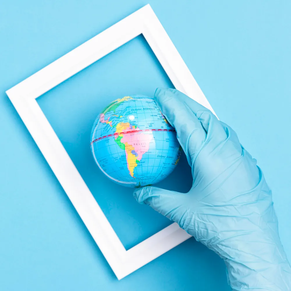 A gloved hand holds a small globe of the Earth, positioned within a white rectangular frame against a light blue background.