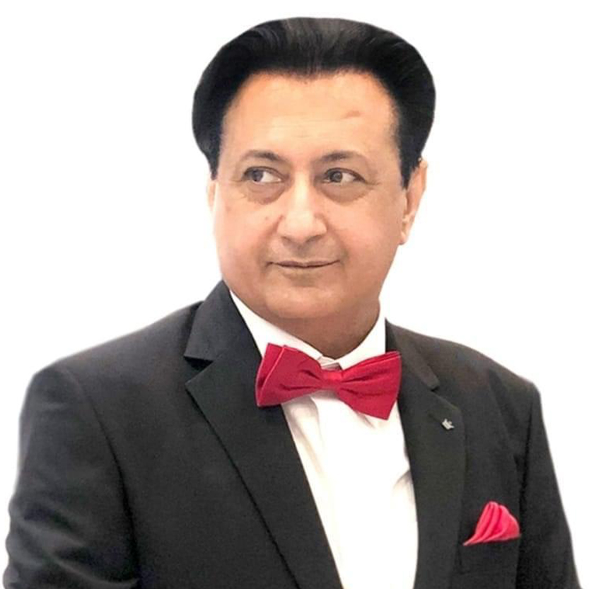 A man in a black suit with a red bow tie and pocket square, looking thoughtfully to his right.